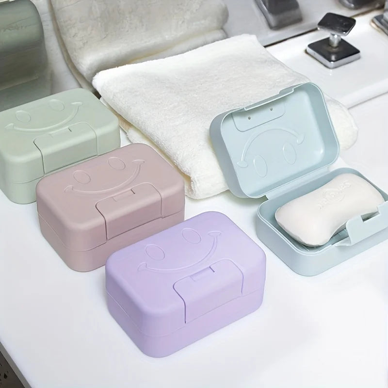 A set of pastel-colored smiley face lidded soap dishes and a white towel are displayed on a white surface.
