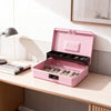 A pink lockable cash box with an open lid displaying coin trays and money inside on a wooden desk.