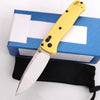 A yellow folding knife with a stainless steel blade is shown resting on a blue box and a black sheath.