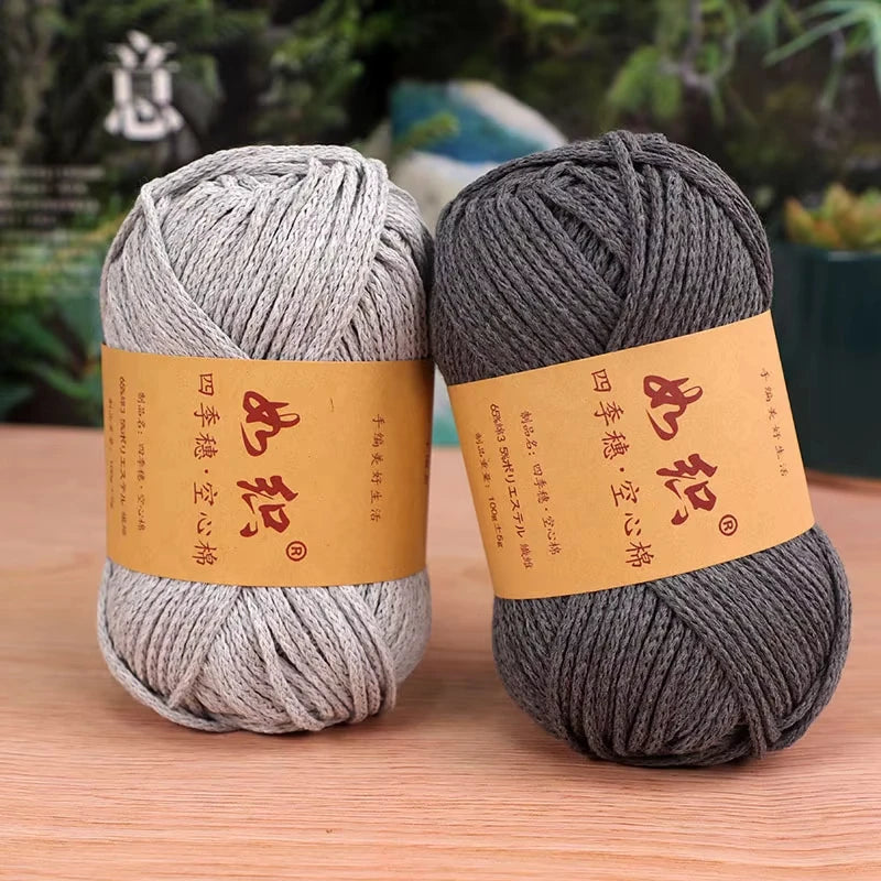 Two skeins of gray cotton blend crochet yarn are displayed on a wooden surface.