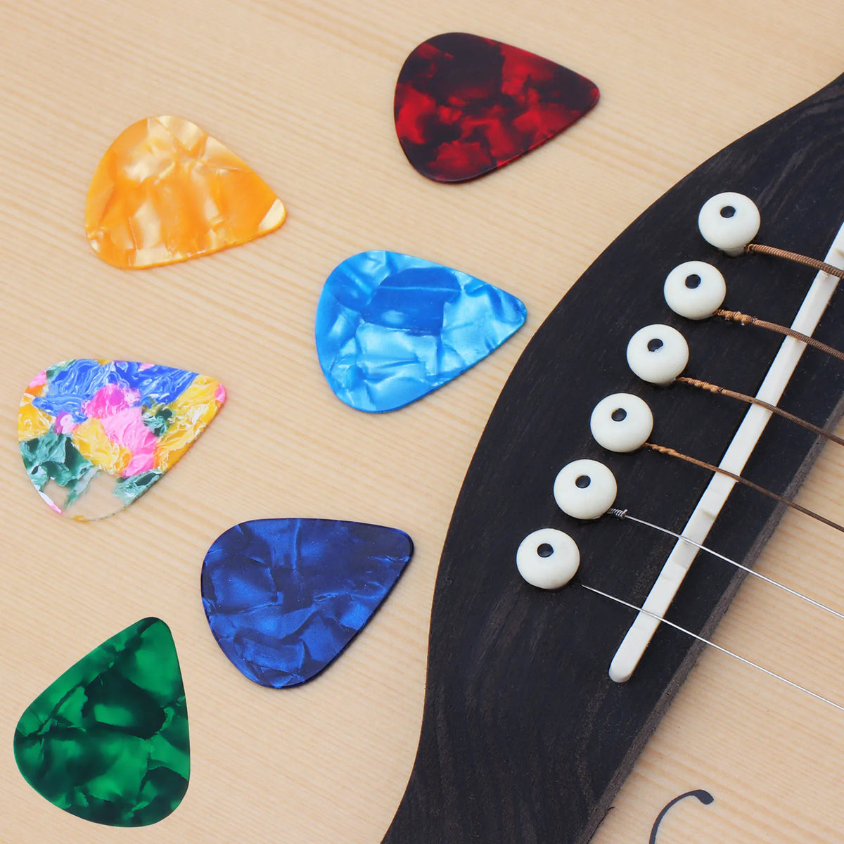 A collection of colorful celluloid guitar picks arranged on a wooden surface next to an acoustic guitar neck.