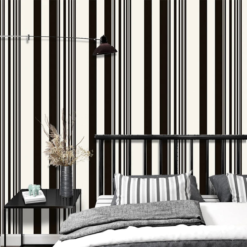 A bedroom setting featuring black and white striped wallpaper, a dark light fixture, and bedding.