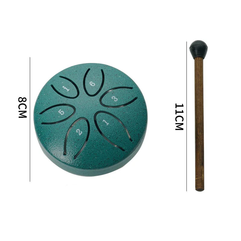 A teal colored mini steel tongue drum with six tuning holes and a wooden mallet shown next to a measurement scale.