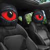 A pair of black and red cartoon eye headrest covers for car seats shown inside a vehicle.