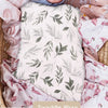 A soft, light pink and green patterned muslin baby swaddle wrap is shown wrapped around a baby's face.