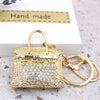 A gold crystal rhinestone handbag keychain resting on a white box with a handmade label.