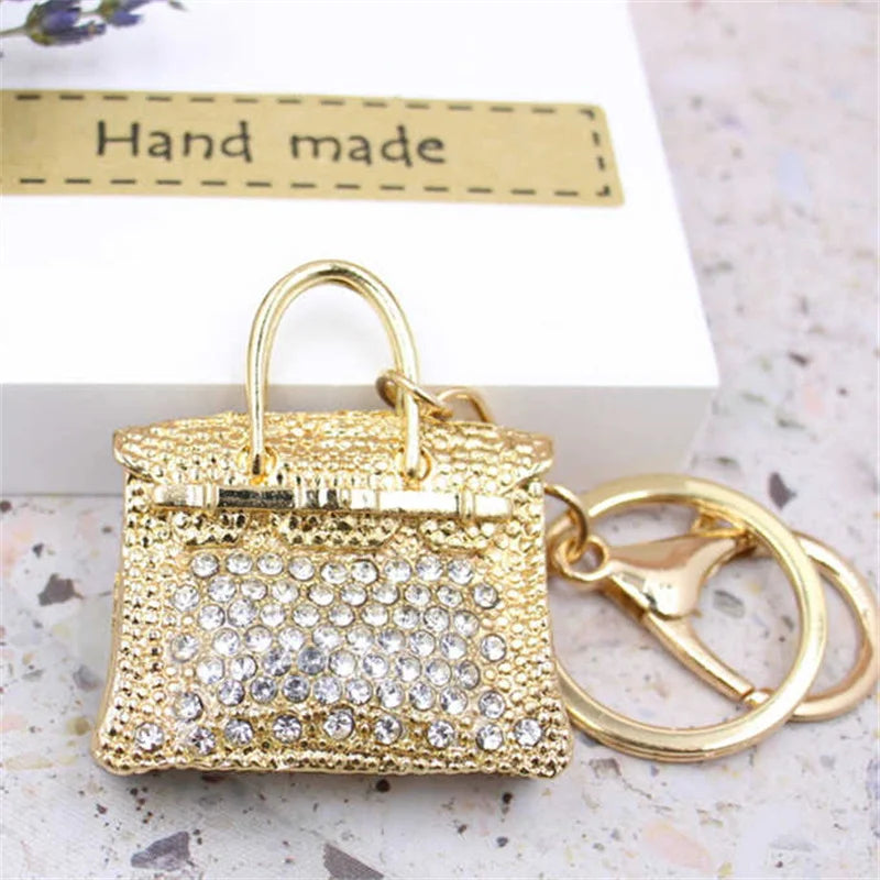 A gold crystal rhinestone handbag keychain resting on a white box with a handmade label.