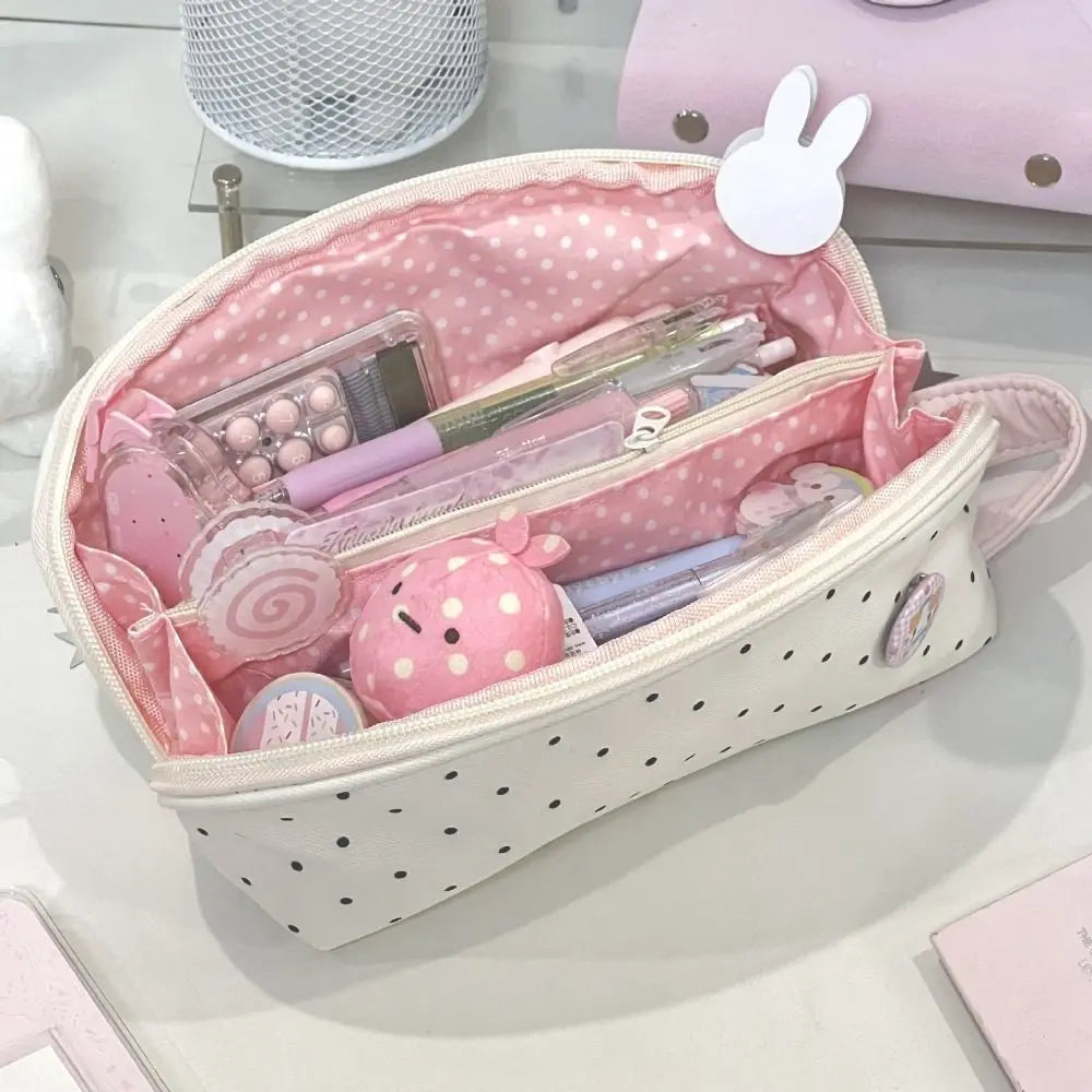 A pink polka dot shell-shaped pencil case with multiple compartments and accessories is shown on a white surface.