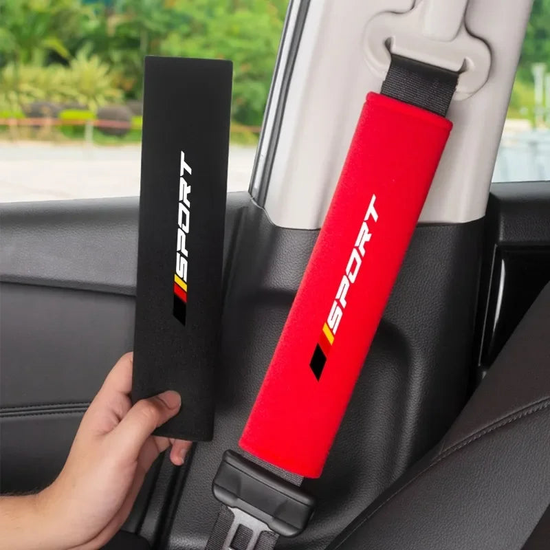 A red and black soft car seat belt cushion is shown installed in a car seat, with another black cushion nearby.