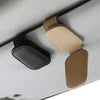 A magnetic leather sunglasses holder with black and tan grips is shown attached to a light gray car sun visor.