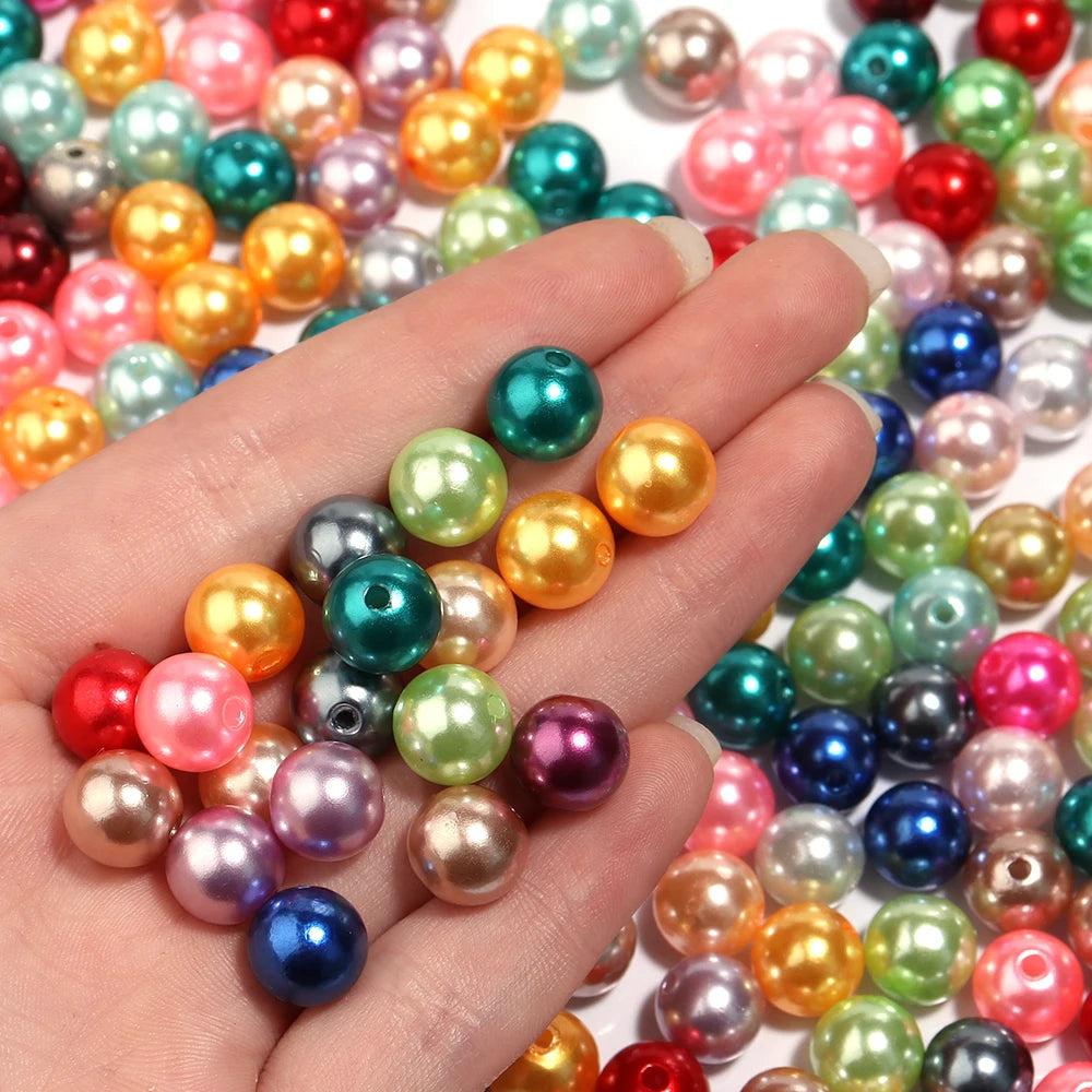 A hand holds a variety of round imitation pearl beads in various colors including pink, green, yellow, and blue.