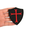 Black shield-shaped embroidered patch featuring a red cross, held in a hand.