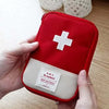 A red pouch with a white cross design is held by a hand, next to a white crocheted container.