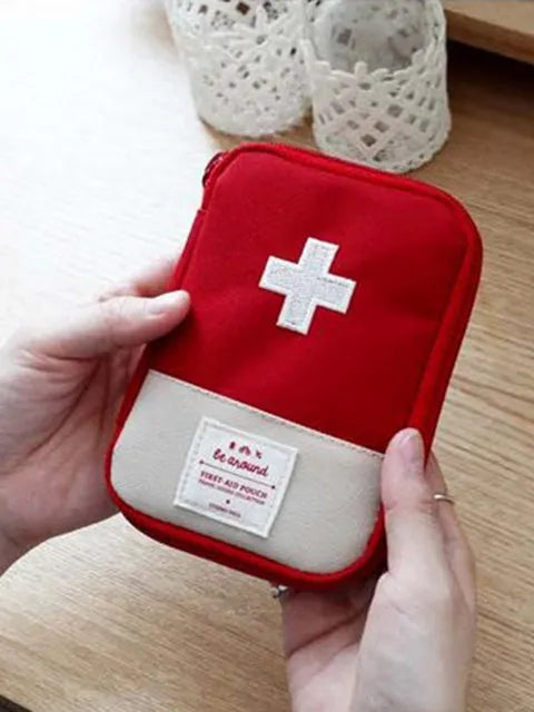 A red pouch with a white cross design is held by a hand, next to a white crocheted container.