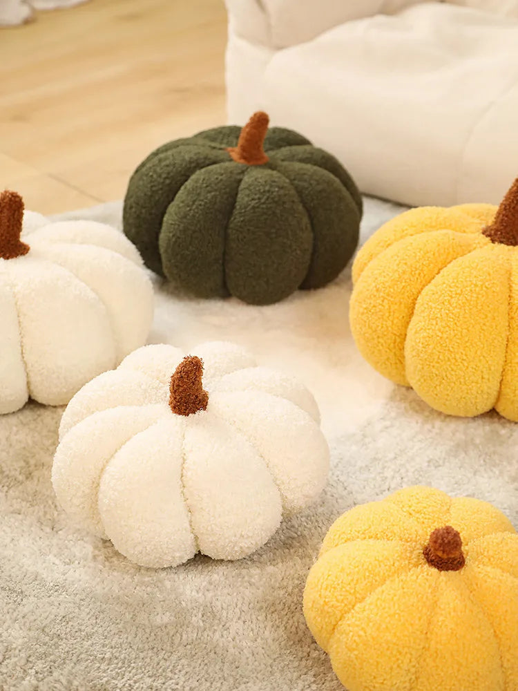 A collection of soft, fuzzy pumpkin-shaped plush cushions in white, green, and yellow resting on a light gray fabric.