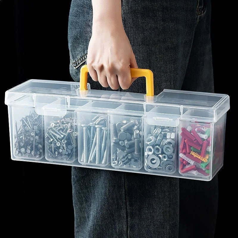 A hand holds a clear plastic multi-compartment tool organizer storage box with yellow handles.