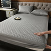 A gray quilted waterproof mattress protector is shown on a bed, with a decorative pillow and a small candle on the surface.