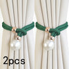 A pair of green rope curtain tie-backs with pearl accents against a light beige curtain.
