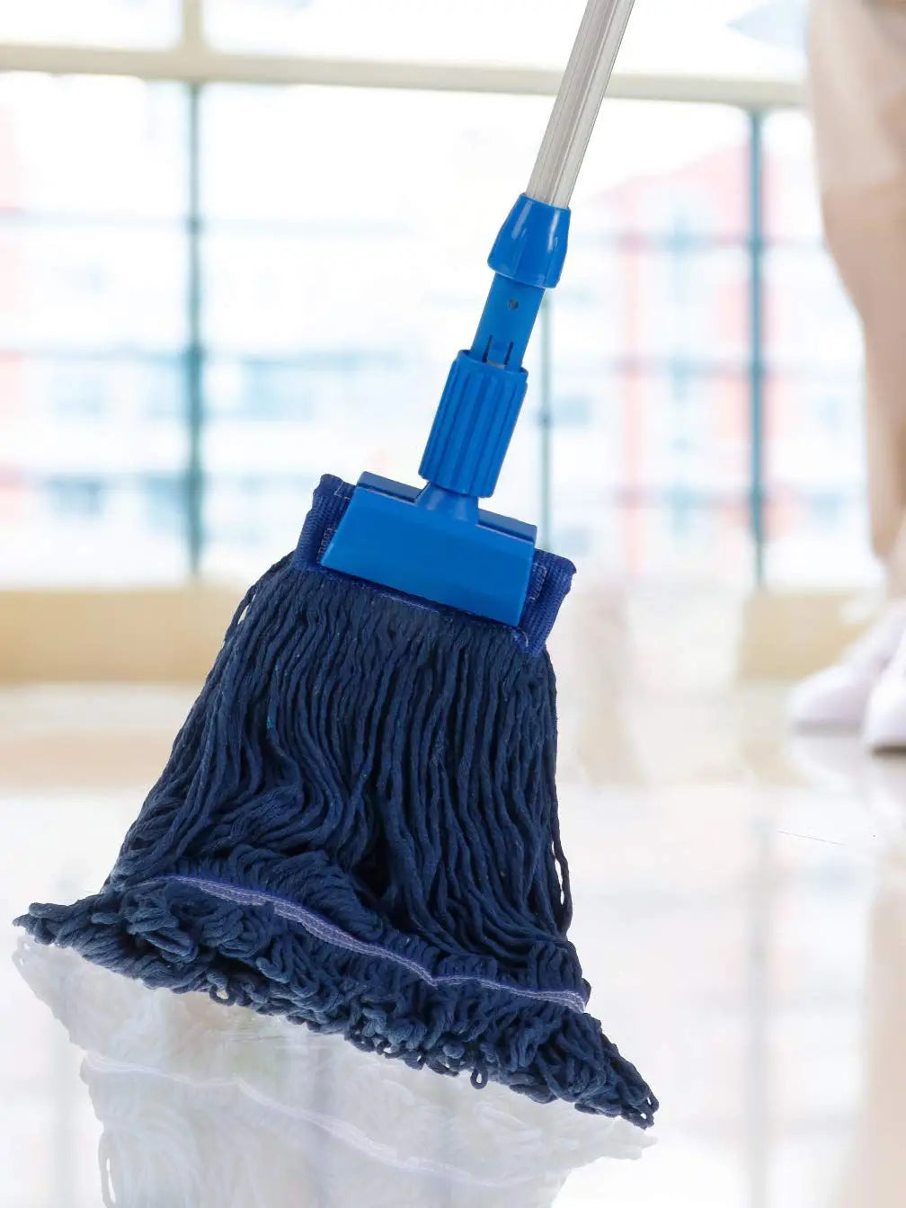 A blue heavy-duty cotton string mop head replacement attached to a white handle, shown in a bright indoor setting.