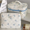 A white quilted cosmetic bag with blue bow print and a light blue zipper, shown next to a smaller matching bag.