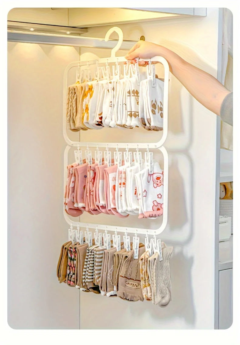 A white multi-clip space-saving laundry drying rack hanging on a closet rod, holding various folded garments.
