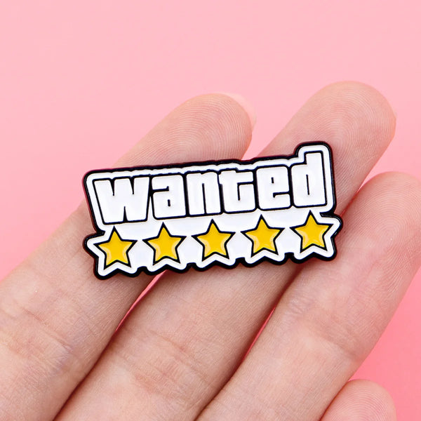 Une main tient une épingle à revers noir et blanc 'wanted' avec quatre étoiles jaunes.