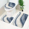 A set of three gray and blue striped bathroom rugs, including a U-shaped toilet mat and cover, placed on a white floor.