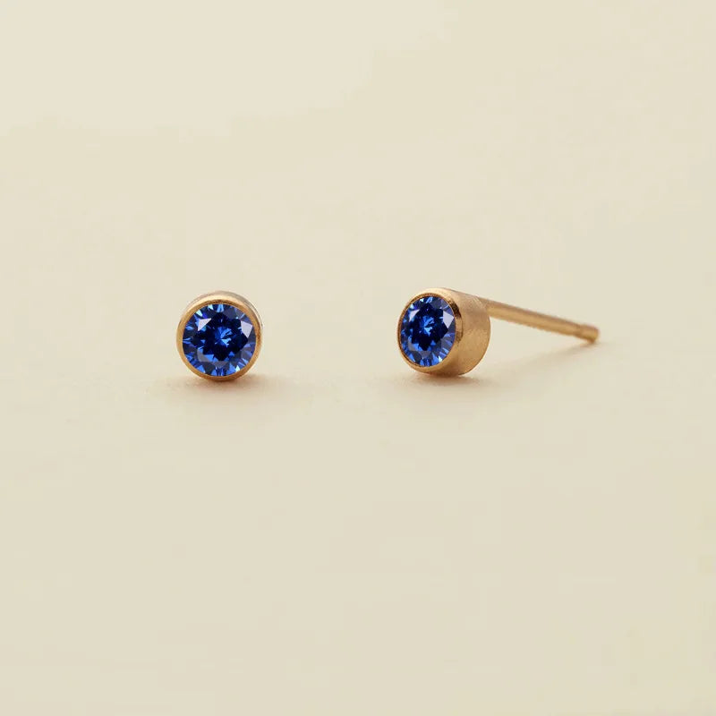 Boucles d'oreilles à studs minimalistes avec des saphirs bleus ronds sur des montures dorées.