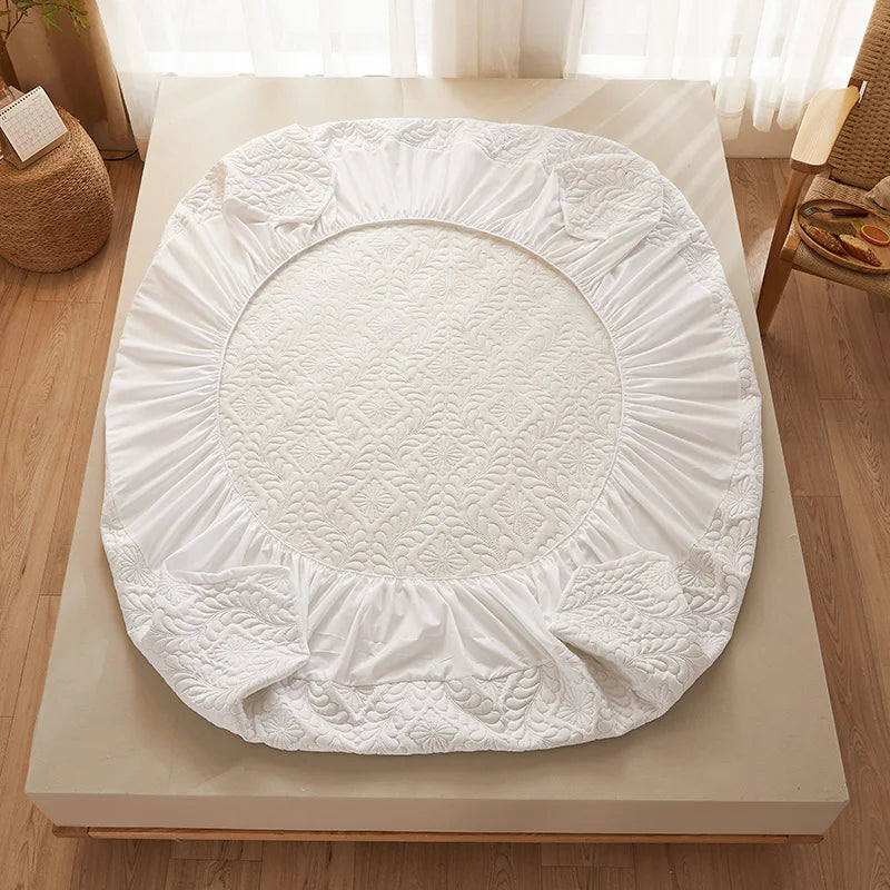 White quilted mattress protector with extra padding placed on a wooden surface.