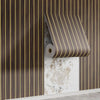 A roll of wood grain peel-and-stick wallpaper in brown and gold stripes is partially unrolled on a vertical wall.