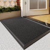 A black non-slip water-resistant doormat with a diamond plate texture placed on a light gray floor in front of a white door.