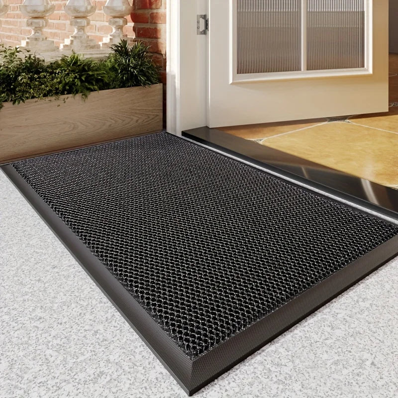 A black non-slip water-resistant doormat with a diamond plate texture placed on a light gray floor in front of a white door.