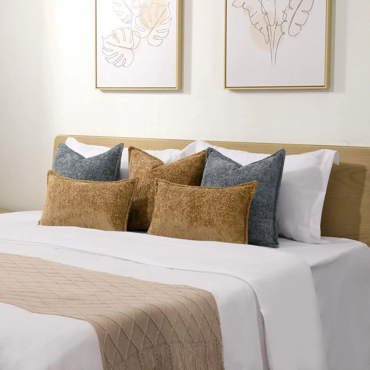 A collection of decorative cushion covers in various shades of gray and gold resting on a white bed with a beige throw blanke