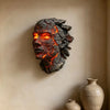 A dark, cracked stone sculpture resembling a face with glowing orange and yellow internal light mounted on a light-colored wa