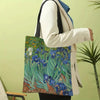 A person holds a canvas tote bag featuring a Van Gogh series painting of blue irises and green foliage.