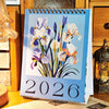 A vertical desk calendar featuring watercolor illustrations of blue and white flowers and the year 2026.