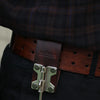 A close-up of a brown leather belt with a bronze buckle and a steel J-hook attached to a black garment.