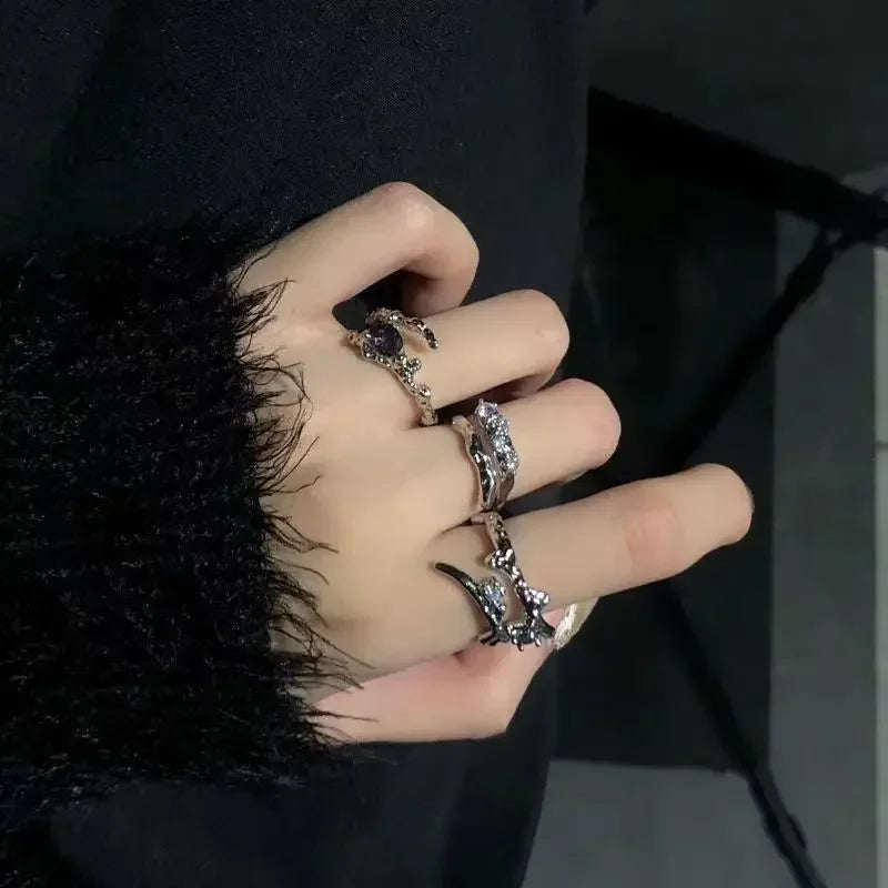 A hand wearing several silver irregular heart-shaped rings on a dark background.