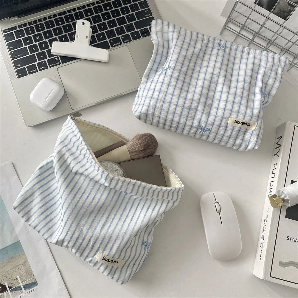 A light blue and white striped makeup bag is shown next to a laptop, a wireless mouse, and a white wireless mouse.
