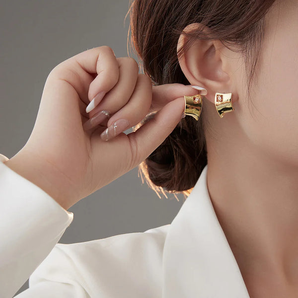 Gros plan d'une main portant des boucles d'oreilles en forme de anneau en turquoise or et argent sur un fond neutre.