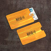 A set of ten yellow RFID protection card sleeves placed on a dark brown surface next to a bank card.
