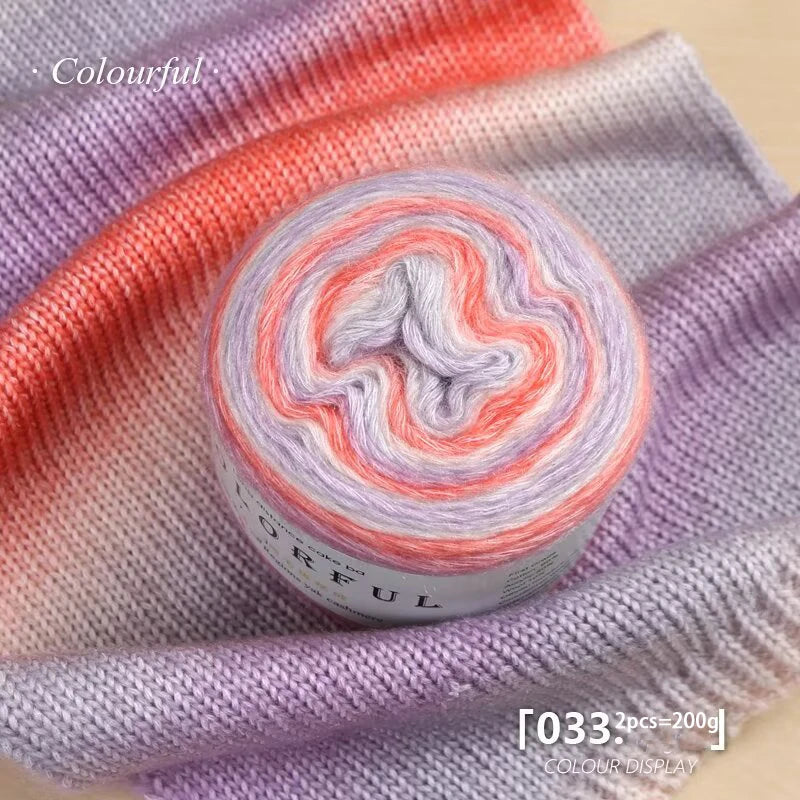 A roll of colorful gradient cake yarn in pink and purple shades displayed on a purple knitted fabric.