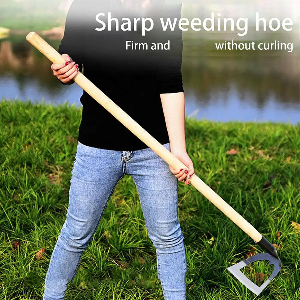 A person holds a sharp weeding hoe with a long wooden handle and metal blade in a grassy outdoor setting.
