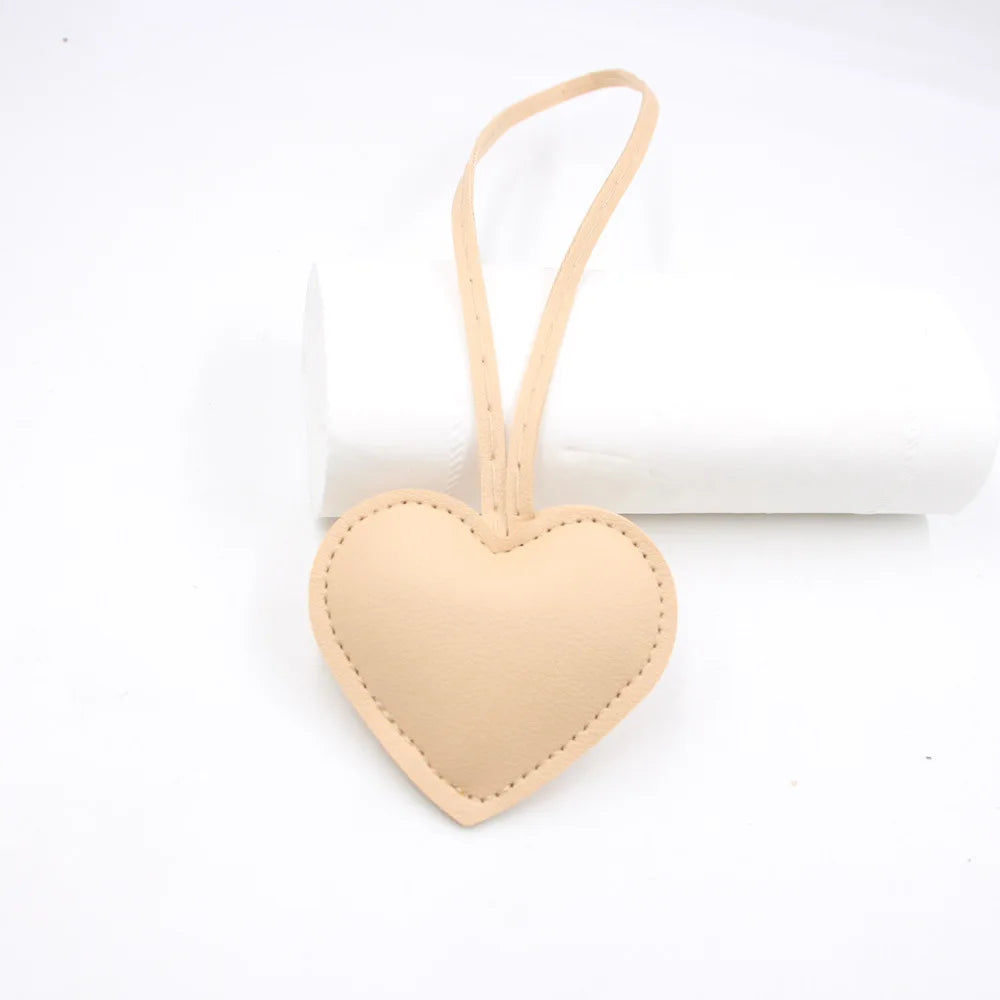 A light peach heart-shaped PU leather keychain with a cotton charm hanging from a loop.