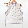 A sleeveless white baby feeding bib with a purple fruit pattern hanging on a wooden hanger.