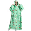 A woman wearing a light green oversized wearable blanket hoodie with a hood and sleeves, featuring small animal patterns.