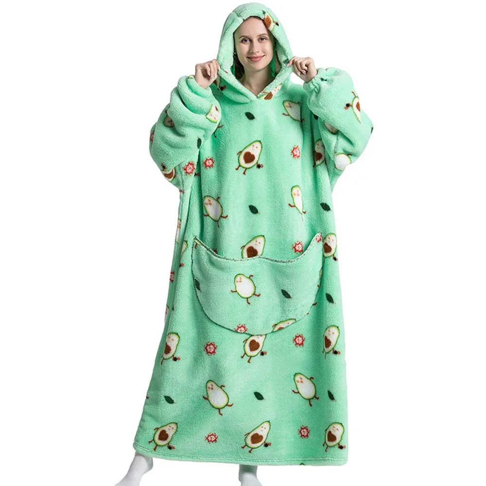 A woman wearing a light green oversized wearable blanket hoodie with a hood and sleeves, featuring small animal patterns.