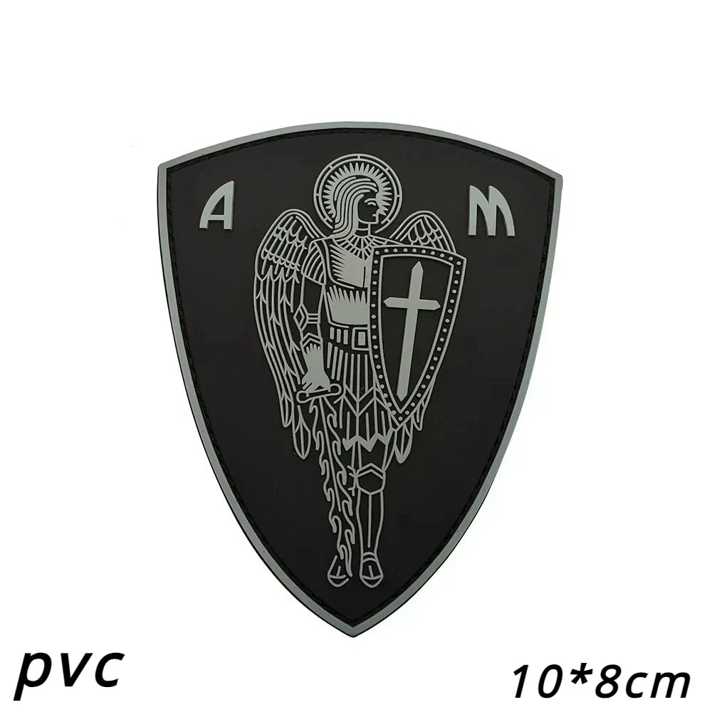 A black shield patch featuring the letters A and M, with an archangel design and a cross emblem.