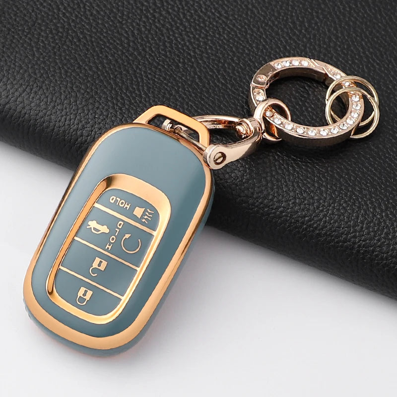 A light blue Honda key fob cover with a gold-tone chain attached, resting on a black surface.