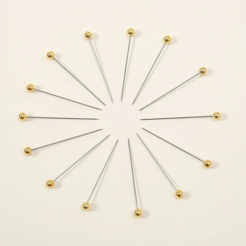 A set of 100 precision quilting pins with gold-colored heads arranged radially on a white background.